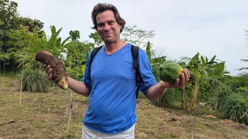 A friend of Dream Village showing fresh harvest from the Dambai food forest — yam in one hand, papaya in the other